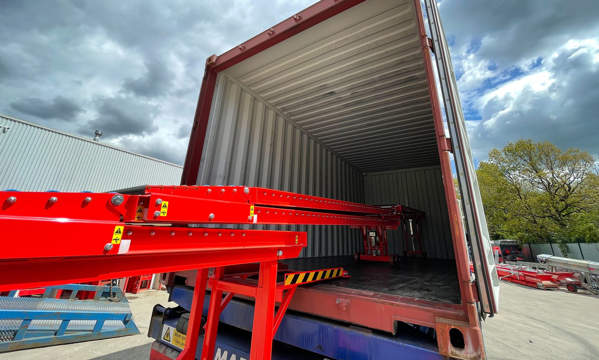 Rulliera telescopica rossa estesa all'interno di un container per lo scarico di merci.
